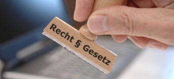Hand hält hölzernen Stempel, auf dem die Worte Recht sowie Gesetz und ein Paragraphen-Zeichen zu sehen sind.
