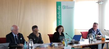Vier Menschen an einem Konferenztisch, dahinter ein Banner der Deutschen Vereinigung für Rehabiliation e.V. Heidelberg.
