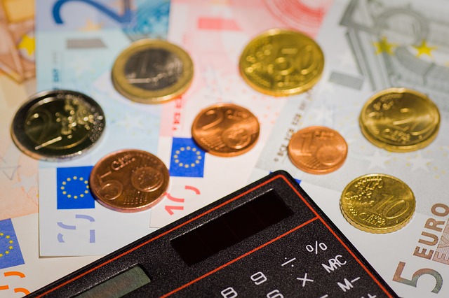 Die Ecke eines Taschenrechners, neben dem zahlreiche Euro-Münzen und -Scheine liegen.