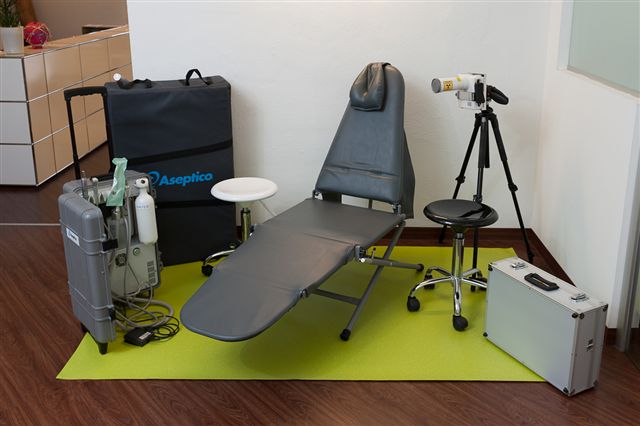 Aufgebaute mobile Zahnarztpraxis mit Behandlungsliege, Arztstuhl und mehreren Koffern mit technischen Geräten.