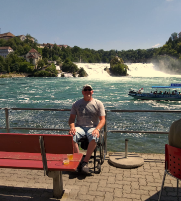 Mann in Rollstuhl im Sonnenschein vor Wasserfällen.