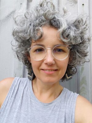 Autorenfoto Barbara Zimmermann mit kurzen, grauen Locken, heller Brille, Nasenring und großen Ohrringen.