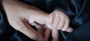Winzige Babayhand umgreift Zeigefinger einer Frauenhand.