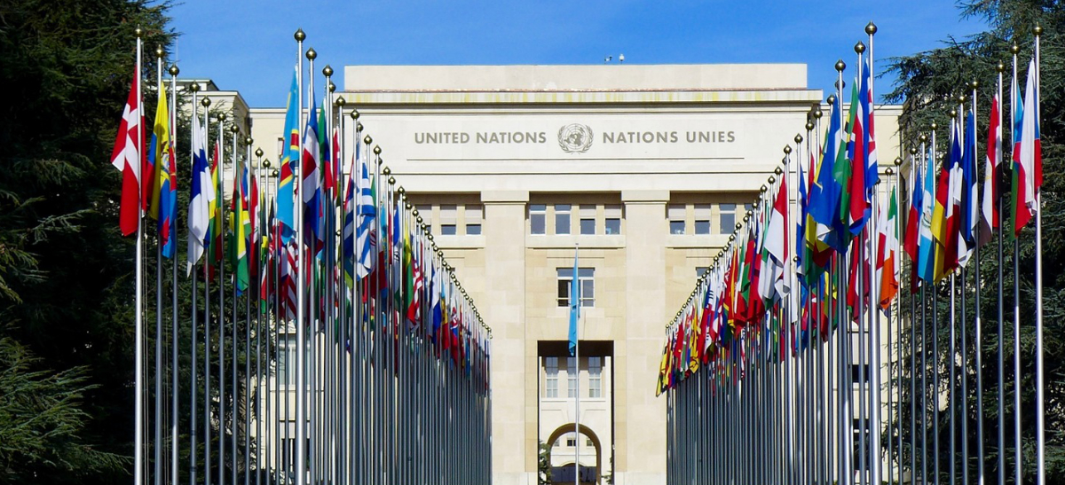 Vorderansicht des Palais des Nations in Genf mit vier langen Flaggen-Reihen.
