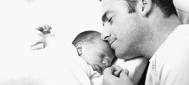Lächelnder Mann legt Wange an Stirn eines schlafenden Babys.