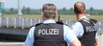 Rückenansicht zweier Polizisten. Auf ihren schwarzen Westen die Aufschrift "Polizei"