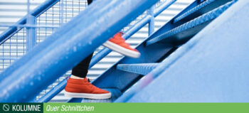 Eine Person mit roten Schuhen und schwarzer Hose geht eine blaue Treppe hinauf. Zu sehen sind nur die Füße und Unterschenkel.