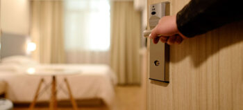 Eine hellbraune Tür öffnet sich in ein helles, freundliches Hotelzimmer, mit weißer Ausstattung.