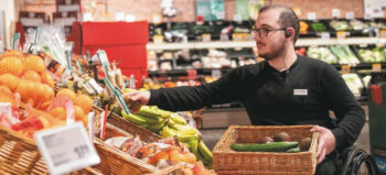 Mitarbeiter im Rollstuhl beim Auffüllen von Gemüse in der Obst- und Gemüseabteilung.