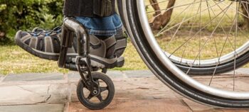 Rollstuhl mit Füßen in grauen Schuhen auf Fußleiste über den Lenkrollen.