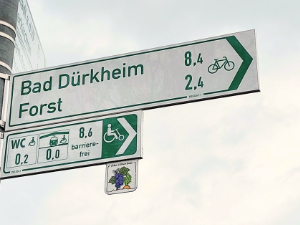 Radwegschilder mit ergänzenden Angaben zur Barrierefreiheit auf der Rüben&Reben-Runde bei Deidesheim: Länge barrierefreier Weg, Entfernung nächster barrierefreier Bahnhof, Entfernung nächstes Behinderten-WC.