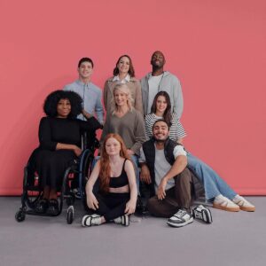 8 männliche und weibliche Models, eines sitzt im Rollstuhl.