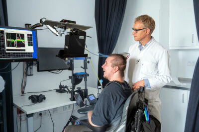 Michael Mehringer und Prof. Simon Jacob beim „Training“ im Labor. Mehringers Kopf ist mit Kabeln mit der Computeranlage verbunden.
