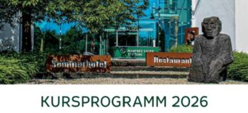 Eingang der Manfred-Sauer-Stiftung mit der zwei Schildern mit der Aufschrift Seminarhotel und Restaurant. An der Seite einer steinerne Figur, die sitzt.