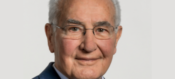 Portraitaufnahme Guido A. Zäch mit weißem Haar und dezenter Brille. Er lächelt freundliche und milde in die Kamera.