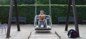 Kleines Kind im Rollstuhl auf öffentlicher Rollischaukel.